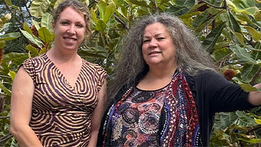 Two women smiling, wearing aboriginal patterned clothing