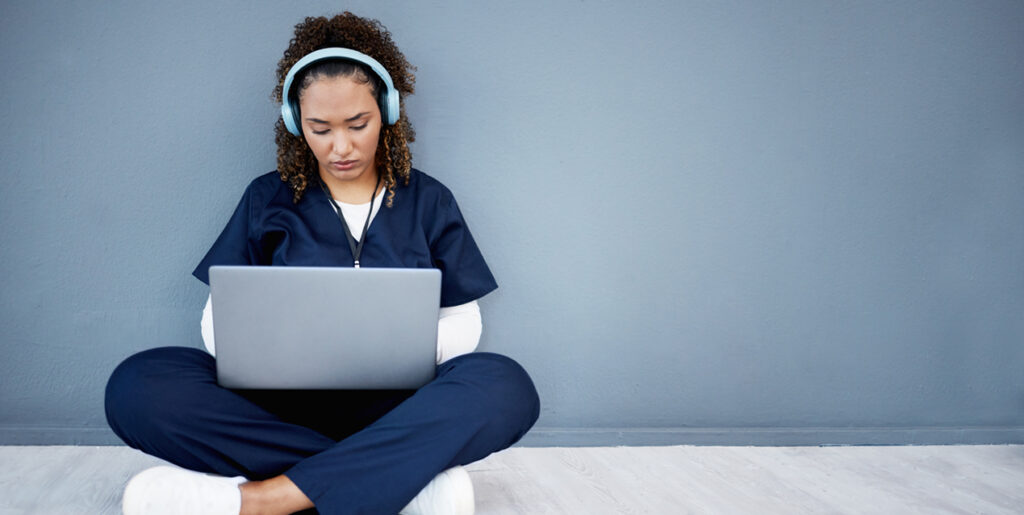Nurse sitting cross legged with laptop on her lap, headphones on